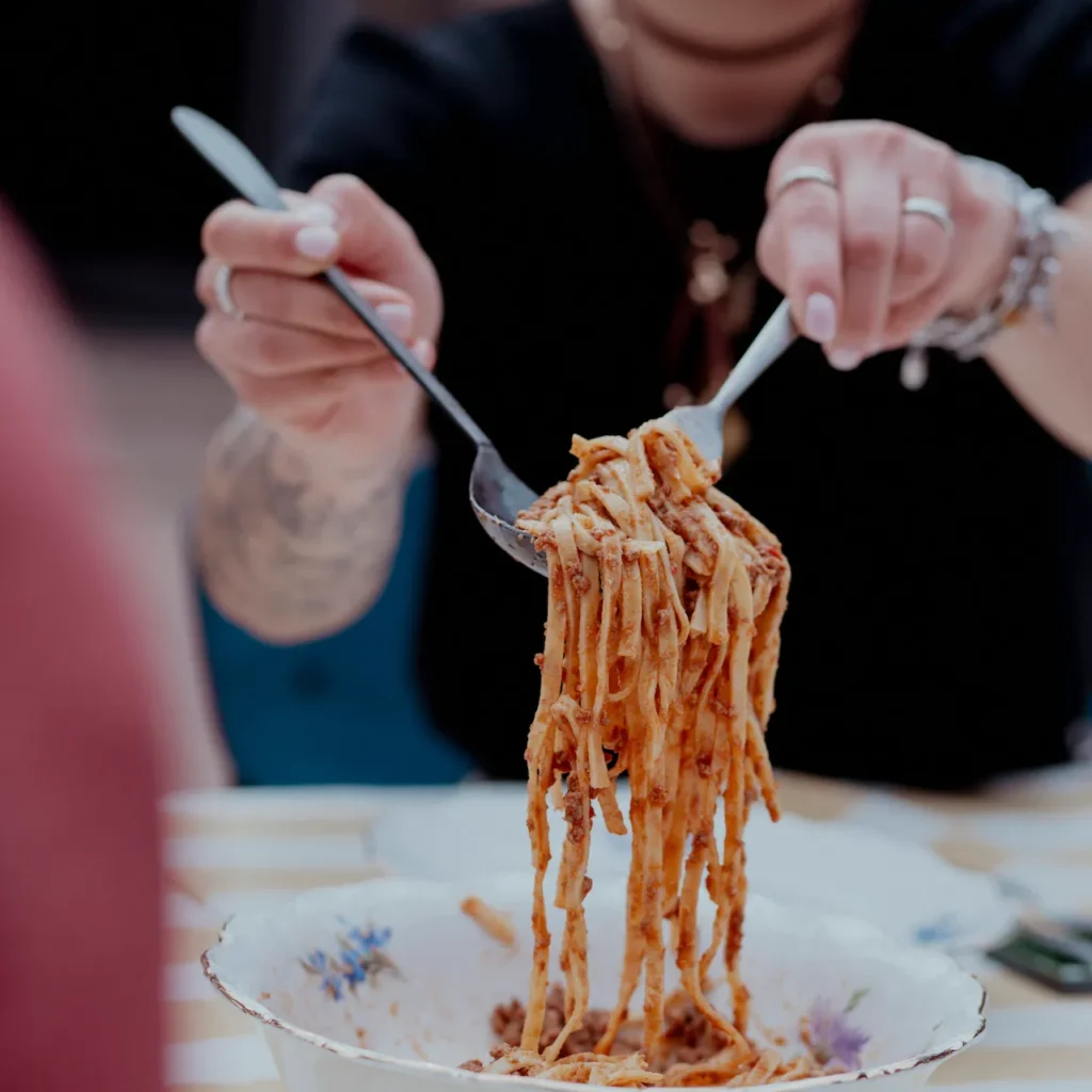 Person serving pasta from a plate during a private dining experience